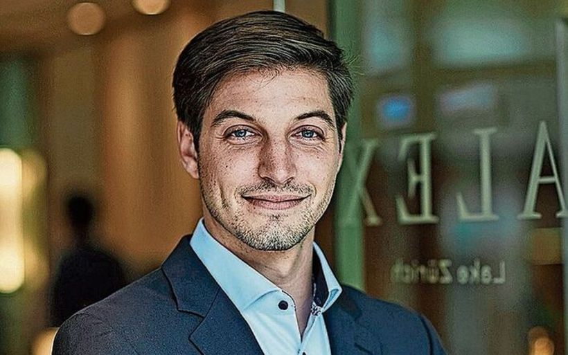 Ein junger Mann steht mit verschränkten Armen vor einer Türe.