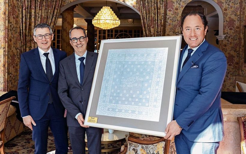 Manuel Küng und Patrik Locatelli von der Schwob AG überreichen Hoteldirektor Heinz E. Hunkeler die 100-jährige Serviette des Kulm Hotel St. Moritz (v. l.).