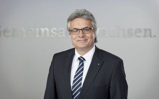 Portrait eines Mannes mittleren Alters mit grauen Haaren und heller Hautfarbe. Er trägt eine Brille und einen Anzug.