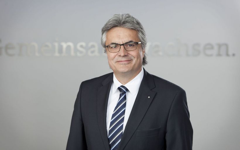 Portrait eines Mannes mittleren Alters mit grauen Haaren und heller Hautfarbe. Er trägt eine Brille und einen Anzug.