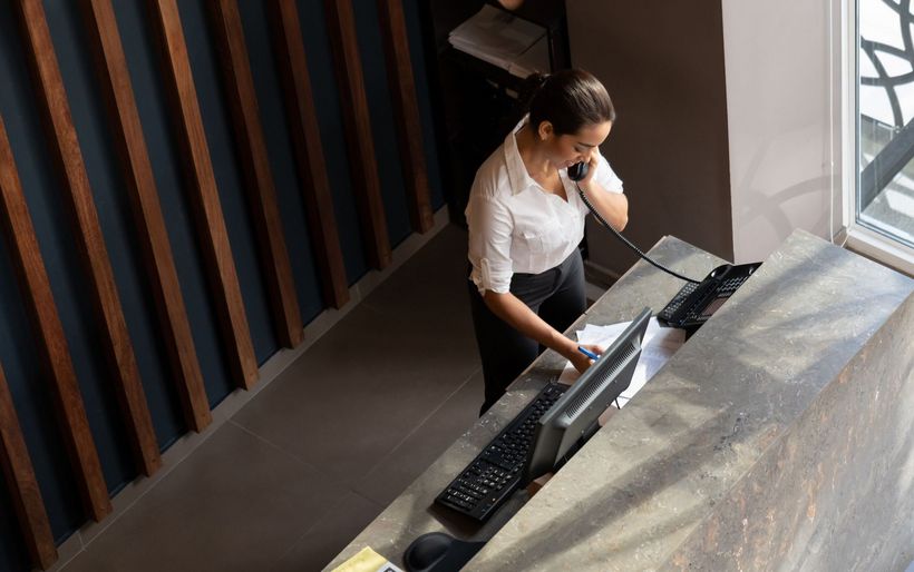 Frau steht an Empfangstresen und telefoneirt.