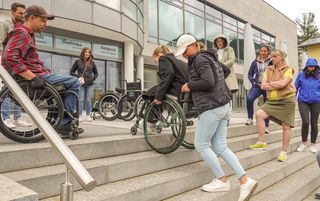 Stephan Gmür (l.) zeigt den Teilnehmenden, wie eine Person im Rollstuhl sicher eine Treppe hinuntergebracht wird.