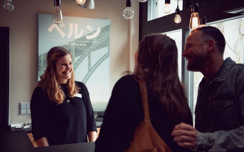 Eine Frau bedient an einer Reception zwei Gäste