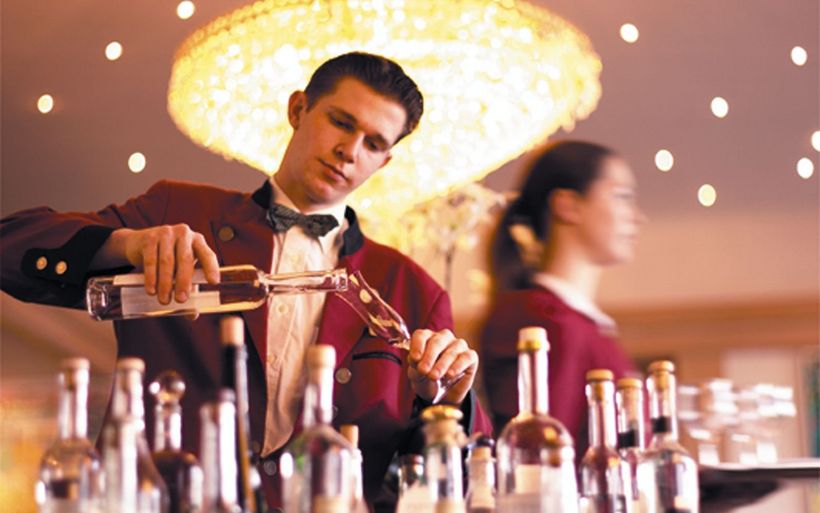 Junger Mann in Service-Arbeitskleidung schenkt ein Getränk ein.